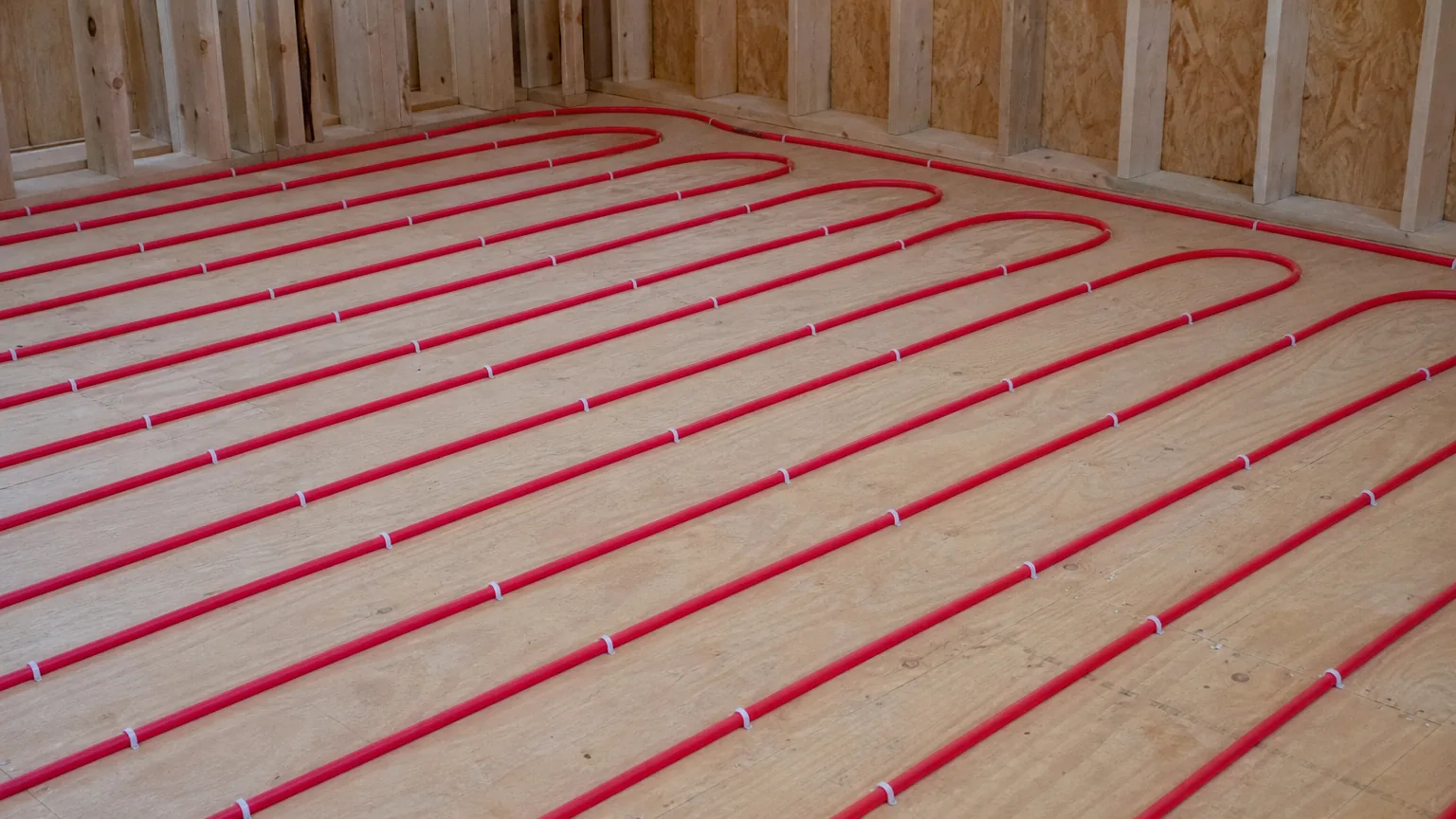 Loops of red PEX tubing clipped to a plywood subfloor