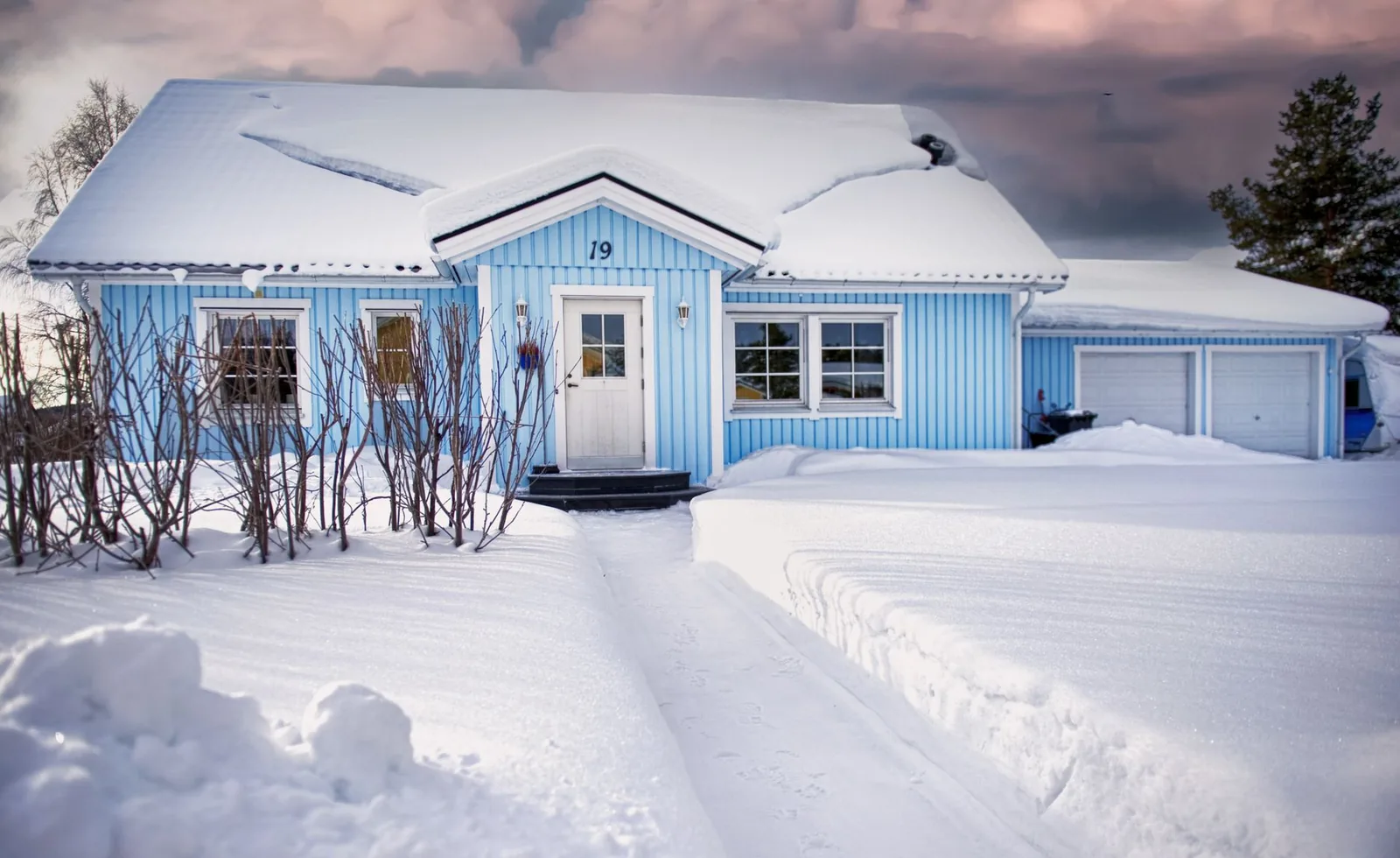 Blue wooden house and driveway buried in deep snow