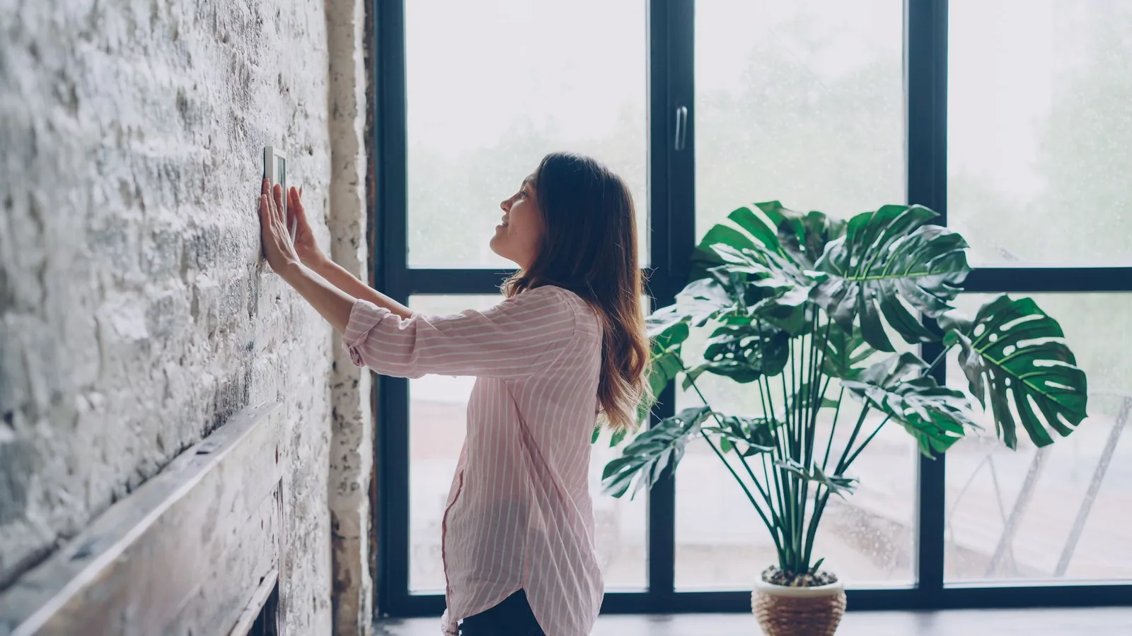 Woman adjusting a thermostat on a brick wall