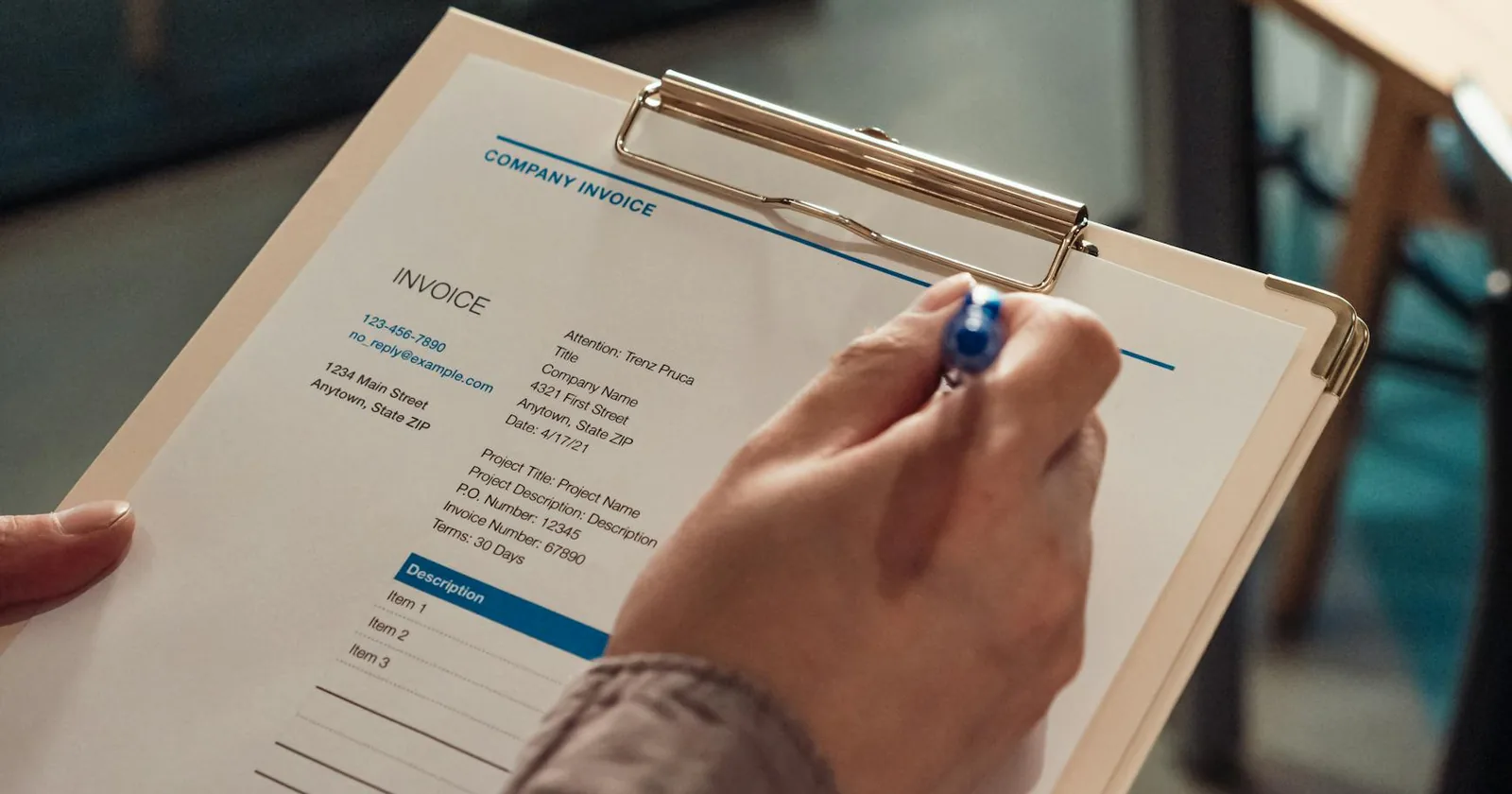 Person's hand holding a company invoice on a clipboard with a pen.