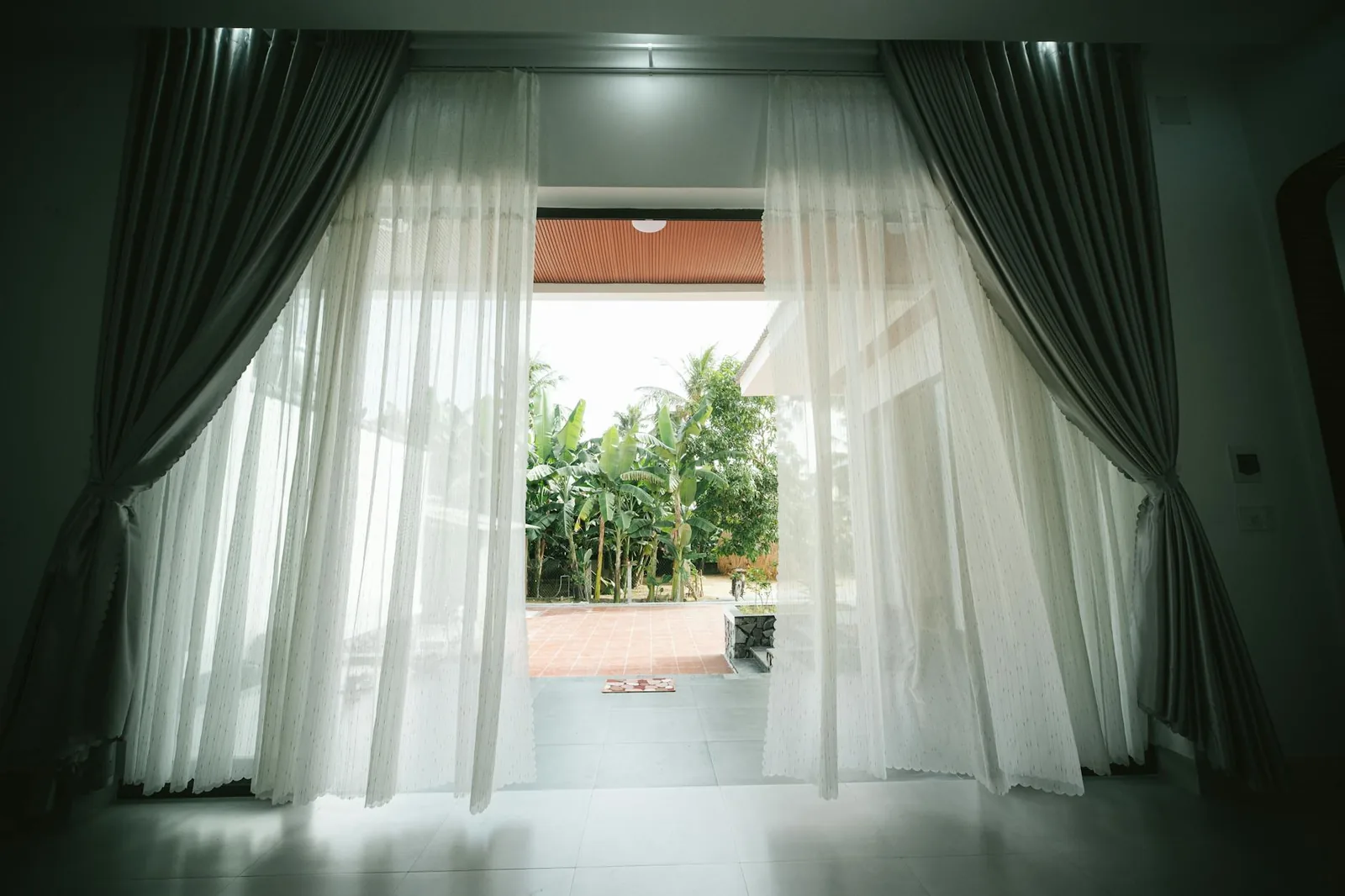 Open doorway with white curtains drawn back, looking out onto a green garden.
