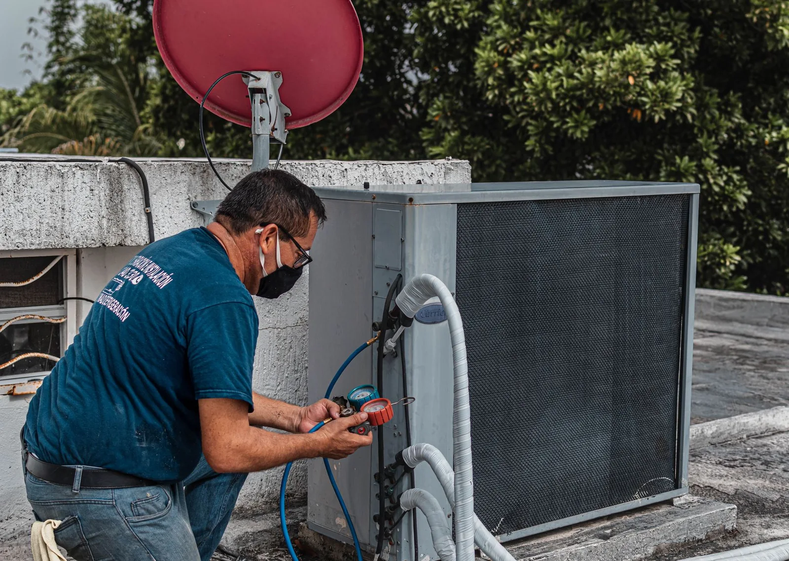 A technician holding manifold gauges at an outdoor AC unit