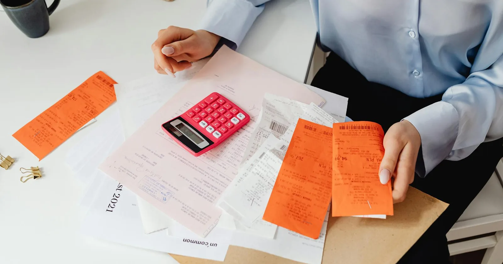 A person reviewing receipts and tallying expenses at a desk with a calculator.