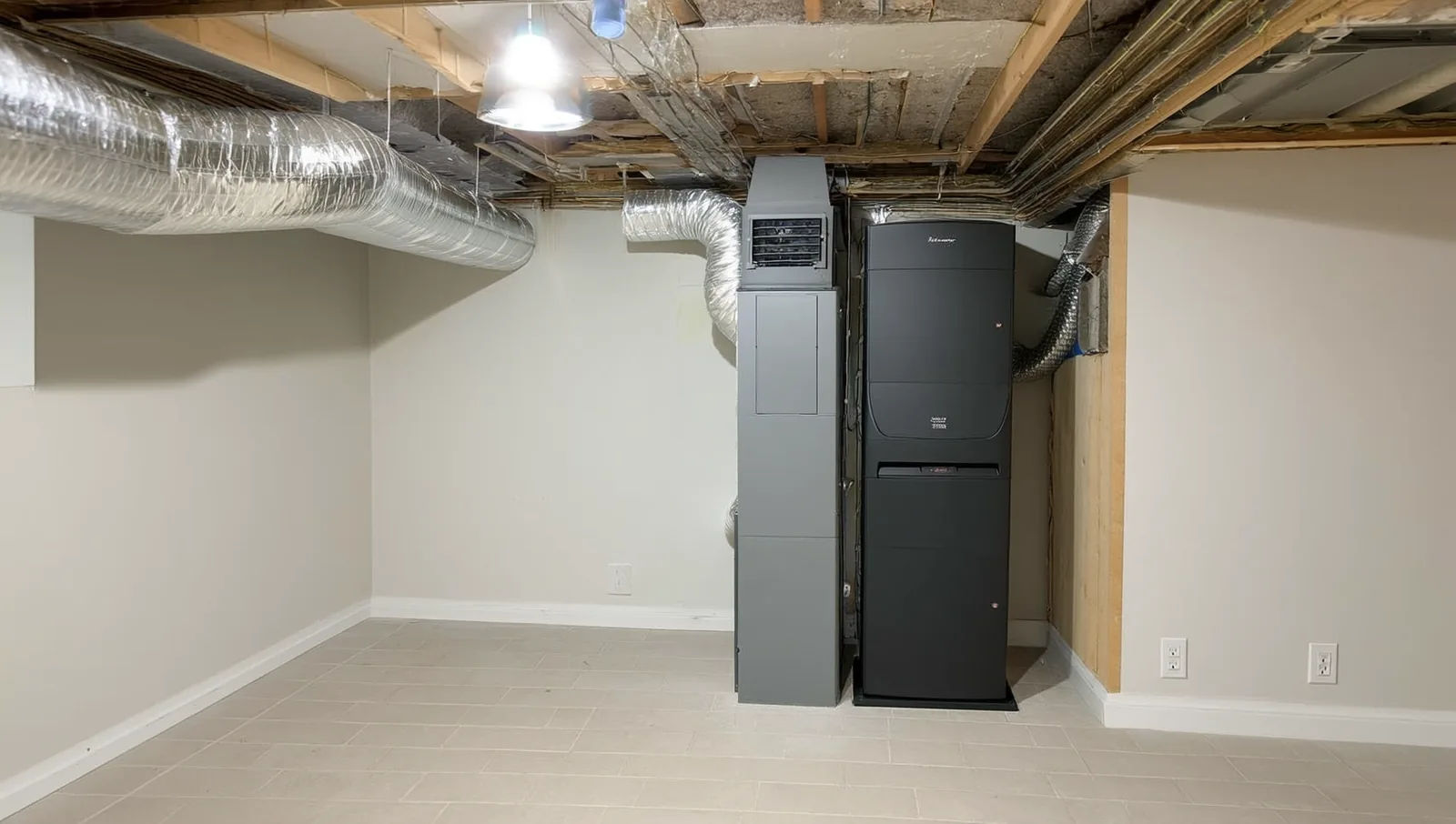 A newly installed high-efficiency gas furnace and air handler in a clean residential basement utility area with sheet metal ductwork overhead.