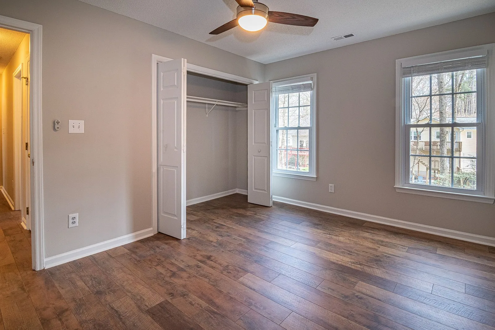 An empty upstairs bedroom with a ceiling fan, a ceiling supply register, and the door standing open to the hallway.